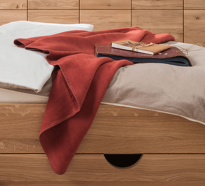 Gemütliche Baumwoll-Plüschdecke auf Bett - hier in rot